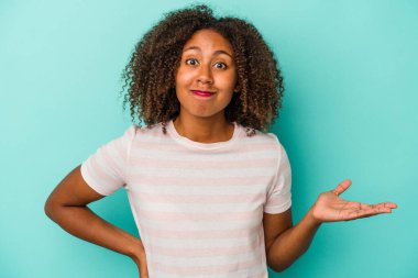 Mavi arka planda izole edilmiş kıvırcık saçlı Afro-Amerikalı genç bir kadın bir avuç içinde fotokopi alanı ve belinde başka bir el tutan.