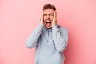 Kafkasyalı genç adam pembe arka planda izole edilmiş kulakları kulaklarıyla kapatıyor çok fazla ses duymamaya çalışıyor..