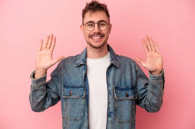 Pembe arka planda izole edilmiş genç beyaz adam on numarayı elleriyle gösteriyor..