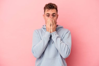 Pembe arka planda izole edilmiş genç beyaz adam elleri endişeli bir şekilde ağzı örtüyor..