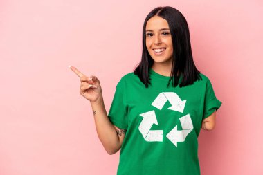 Bir kolu geri dönüştürülmüş, pembe arka planda izole edilmiş beyaz bir kadın gülümsüyor ve boş alanda bir şey gösteriyor..