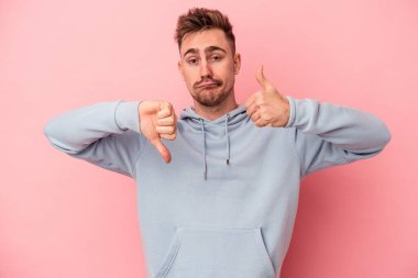 Pembe arka planda izole edilmiş genç beyaz bir adam baş parmağını kaldırıyor ve baş parmağıyla işaret ediyor. Zor bir seçim.