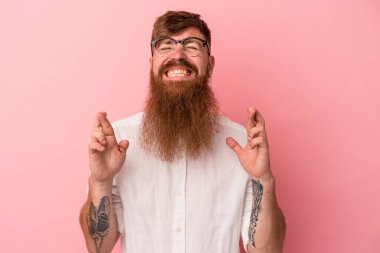 Uzun sakallı, beyaz tenli genç adam şans dilemek için pembe arka planda izole edildi.
