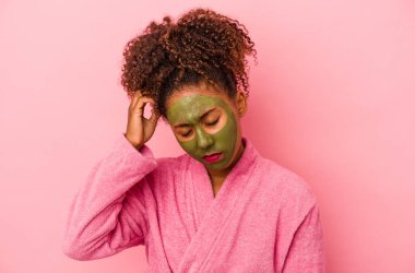 Bornoz ve yüz maskesi takan genç Afro-Amerikalı kadın pembe arka planda izole edilmiş şok geçiriyordu..