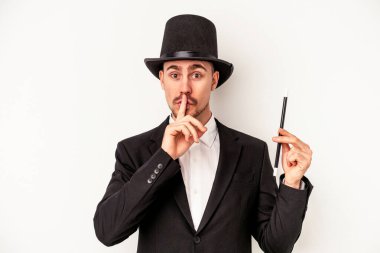 Beyaz arka planda bir değnek tutan genç beyaz büyücü ya sır saklıyor ya da sessizlik istiyor..