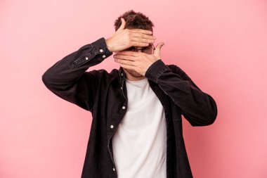Pembe arka planda izole edilmiş genç beyaz adam kameraya parmaklarıyla göz kırpıyor, yüzünü kapatmaktan utanıyor..