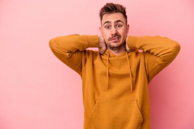 Kafkasyalı genç bir adam pembe arka planda izole edilmiş kafasının arkasına dokunuyor, düşünüyor ve bir seçim yapıyor..