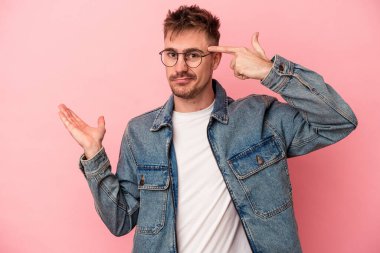 Pembe arka planda izole edilmiş genç beyaz adam elinde bir ürün tutuyor..