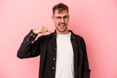 Pembe arka planda izole edilmiş genç beyaz bir adam gömlek fotokopi alanını elle gösteriyor, gururlu ve kendinden emin.