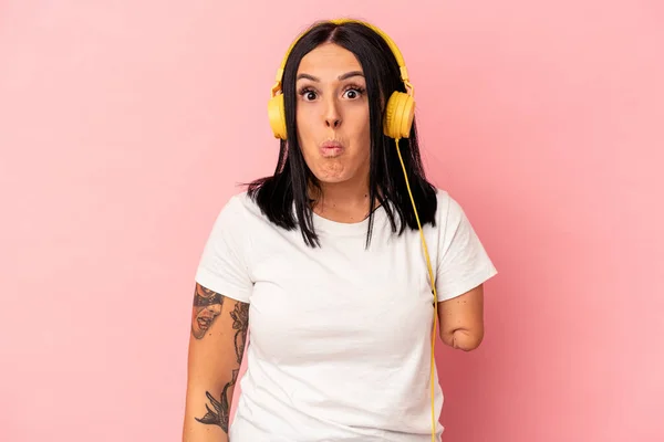 Young caucasian woman with one arm listening to music isolated on pink background shrugs shoulders and open eyes confused.