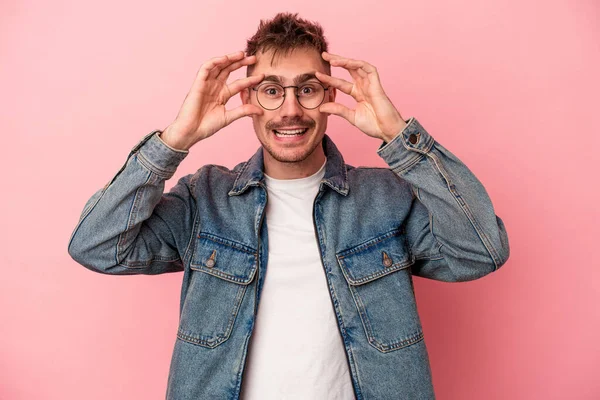 Pembe arka planda izole edilmiş genç beyaz adam bir başarı fırsatı bulmak için gözlerini açık tutuyor..