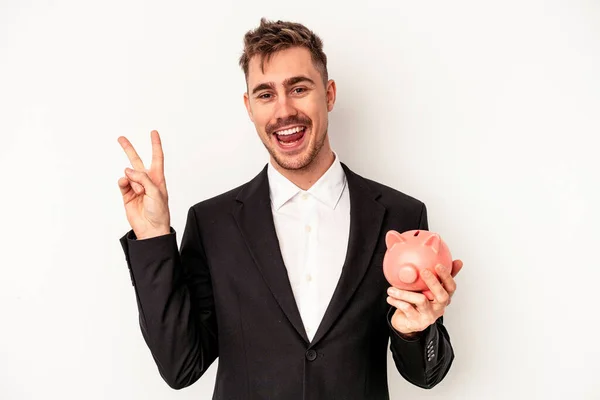 白を基調とした貯金箱を持つ若い白人実業家は喜びと屈託なく指で平和の象徴を示す — ストック写真