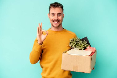 Beyaz bir genç, mavi arka planda izole edilmiş, neşeli ve kendinden emin bir şekilde hareket ediyor..