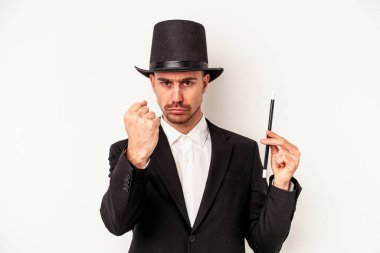 Beyaz arka planda bir değnek tutan genç beyaz büyücü kameraya yumruk gösteriyor, agresif yüz ifadesi..