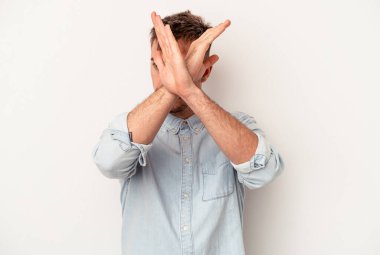 Beyaz arka planda izole edilmiş genç beyaz adam elleriyle ağzını kapatırken şok oldu..