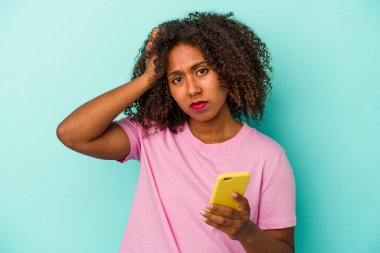 Mavi arka planda cep telefonu tutan genç Afrikalı Amerikalı kadın şok geçiriyordu..