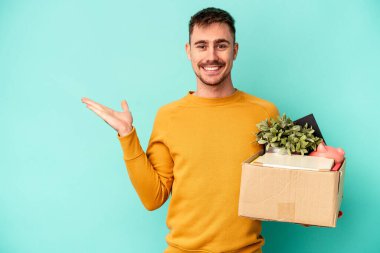 Kafkasyalı genç bir adam mavi arka planda izole edilmiş bir hareket yapıyor. Bir avuç içinde fotokopi alanı ve belinde başka bir el tutuyor..