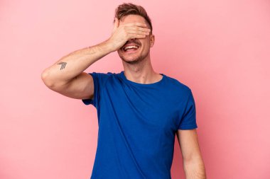 Pembe arka planda soyutlanmış genç beyaz adam elleriyle gözlerini kapatıyor, geniş bir gülümsemeyle bir sürpriz bekliyor..