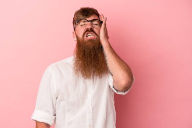 Uzun sakallı, beyaz, genç bir adam pembe arka planda izole edilmiş. Yorgun ve uykulu. Elini başının üstünde tutuyor..