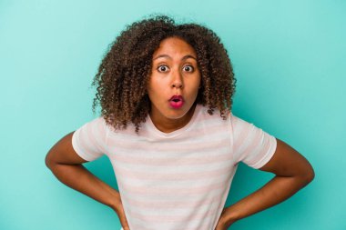 Mavi arka planda izole edilmiş kıvırcık saçlı genç Afro-Amerikalı kadın gördüğü bir şey yüzünden şoka uğruyor..