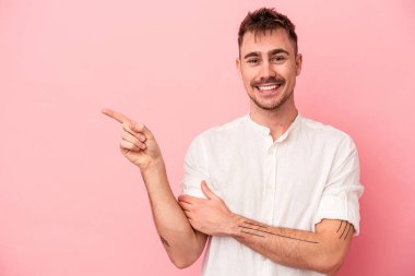 Pembe arka planda izole edilmiş genç beyaz adam işaret parmağıyla işaret ederek gülümsüyor..