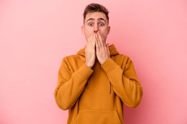Pembe arka planda izole edilmiş genç beyaz adam elleriyle ağzını kapatırken şok oldu..
