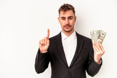 Elinde banknotlar tutan Kafkasyalı genç bir iş adamı beyaz arka planda bir numarayı parmağıyla gösteriyor..
