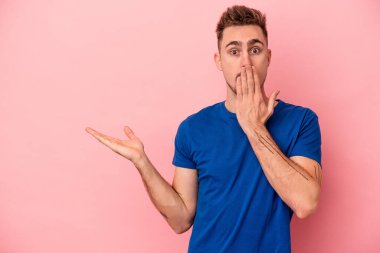 Pembe arka planda izole edilmiş genç beyaz adam, avuç içi fotokopi alanını elinde tutmaktan etkilenmiş..