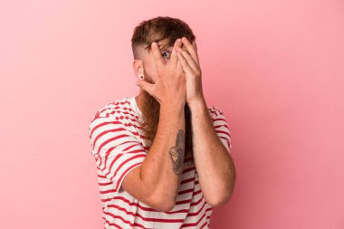 Pembe arka planda, uzun sakallı, beyaz, genç bir adam. Korkmuş ve gergin parmaklarıyla göz kırp..