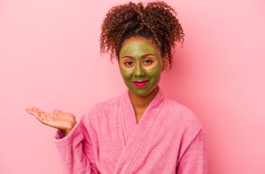 Pembe arka planda, bornoz ve yüz maskesi takan Afro-Amerikalı genç bir kadın bir avuç içinin fotokopi çektiğini ve belinde bir el daha tuttuğunu gösteriyor..