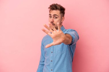 Pembe arka planda izole genç beyaz adam yakın bir tehlike nedeniyle şoka uğruyor.