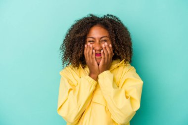 Mavi arka planda yalıtılmış kıvırcık saçlı, genç Afro-Amerikalı bir kadın bir şeye gülüyor, elleriyle ağzını kapatıyor..