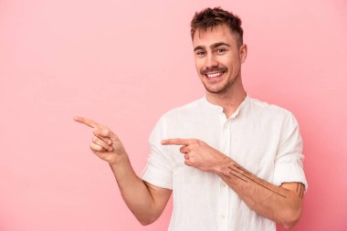 Pembe arka planda izole edilmiş genç beyaz adam işaret parmağıyla işaret ederek heyecanlanıyor..