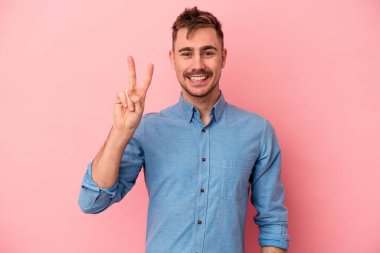 Pembe arka planda izole edilmiş genç beyaz adam iki numarayı parmaklarıyla gösteriyor..