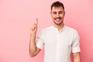 Pembe arka planda izole edilmiş genç beyaz bir adam bir numarayı parmağıyla gösteriyor..