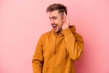 Pembe arka planda izole edilmiş genç beyaz adam bir dedikoduyu dinlemeye çalışıyor..