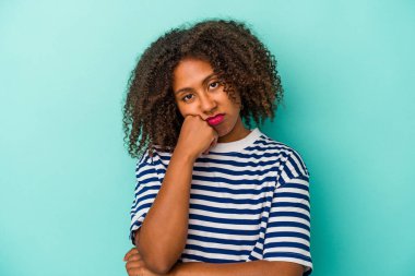 Mavi arka planda izole edilmiş kıvırcık saçlı, üzgün ve dalgın hisseden ve fotokopi odasına bakan Afro-Amerikan genç kadın..