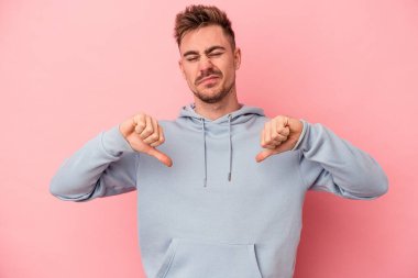 Pembe arka planda izole edilmiş genç beyaz adam baş parmağını aşağı gösteriyor, hayal kırıklığı konsepti..