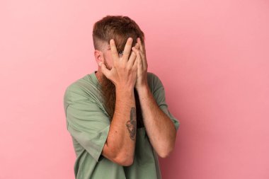 Pembe arka planda, uzun sakallı, beyaz, genç bir adam. Korkmuş ve gergin parmaklarıyla göz kırp..