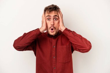 Beyaz arka planda izole edilmiş genç beyaz bir adam uzaklara bakıyor ve elini alnına koyuyor..