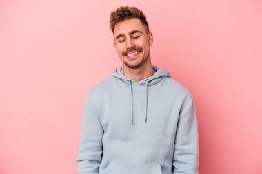 Pembe arka planda izole edilmiş genç beyaz adam gülüyor ve gözlerini kapıyor, rahatlamış ve mutlu hissediyor..