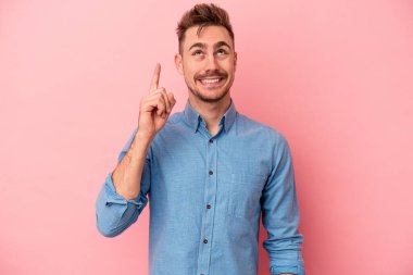 Pembe arka planda izole edilmiş genç beyaz adam iki parmağı da boş bir alan gösteriyor..