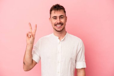 Pembe arka planda izole edilmiş genç beyaz adam zafer işareti gösteriyor ve gülümsüyor..
