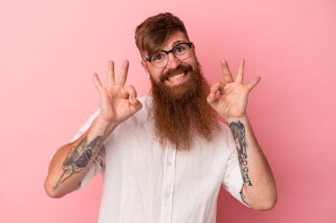Uzun sakallı, beyaz tenli genç adam pembe arka planda izole edilmiş neşeli ve kendinden emin..