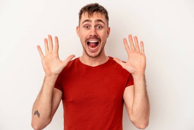 Beyaz arka planda izole edilmiş beyaz tenli genç bir adam parmakları dudaklarında bir sır saklıyor..