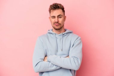Pembe arka planda izole edilmiş genç beyaz adam alaycı bir ifadeyle kameraya bakıyor..