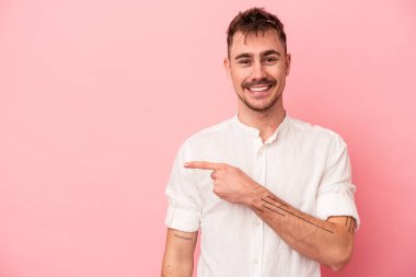 Pembe arka planda izole edilmiş genç beyaz adam gülümsüyor ve boş alanda bir şeyler gösteriyor..