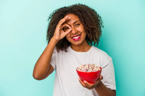 年轻的非洲裔美国女人拿着一碗蓝色背景的谷类食物 兴奋得目瞪口呆 — 图库照片