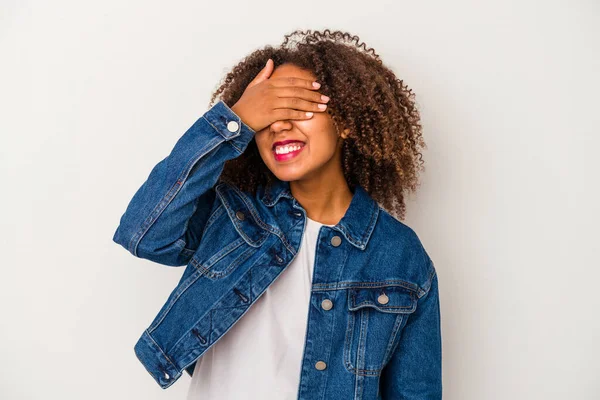 Beyaz arka planda yalıtılmış kıvırcık saçlı, genç Afro-Amerikalı kadın gözleri kaplıyor, gülümseyerek büyük bir sürpriz bekliyor..
