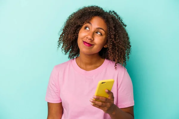 Młoda Afroamerykanka Trzymająca Telefon Komórkowy Niebieskim Tle Marząca Osiągnięciu Celów — Zdjęcie stockowe